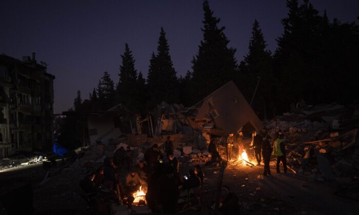 Những người bạn và người thân của gia đình Daghli quây quần bên đống lửa trong khi đội cứu hộ tìm kiếm các thành viên trong gia đình dưới đống đổ nát của một tòa nhà bị phá hủy ở Antakya, đông nam Thổ Nhĩ Kỳ, hôm 15/02/2023. (Ảnh: Bernat Armangue/AP Photo)