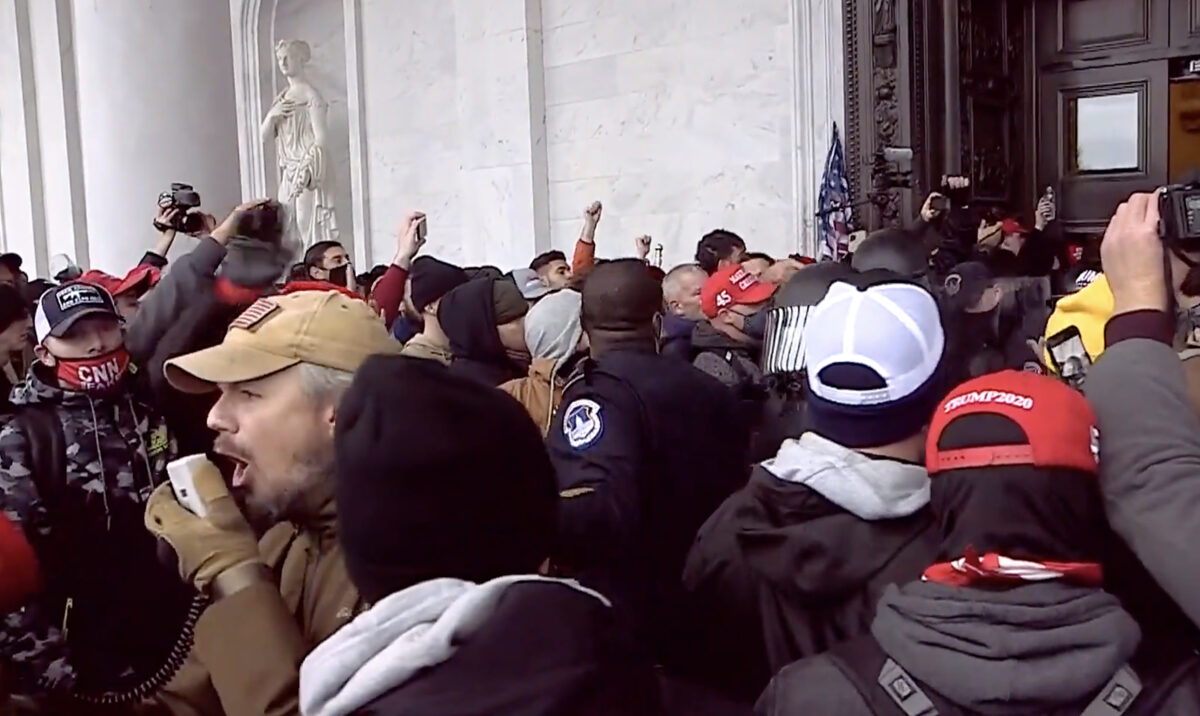 Trung sĩ cảnh sát đã về hưu và là thành viên của tổ chức Oath Keepers, ông Michael Nichols, sử dụng một chiếc loa để tạo lối đi cho các sĩ quan cảnh sát mà ông đang giúp đưa ra khỏi Điện Capitol vào ngày 06/01/2021. (Ảnh: Bộ Tư pháp Hoa Kỳ/Ảnh chụp màn hình qua The Epoch Times)