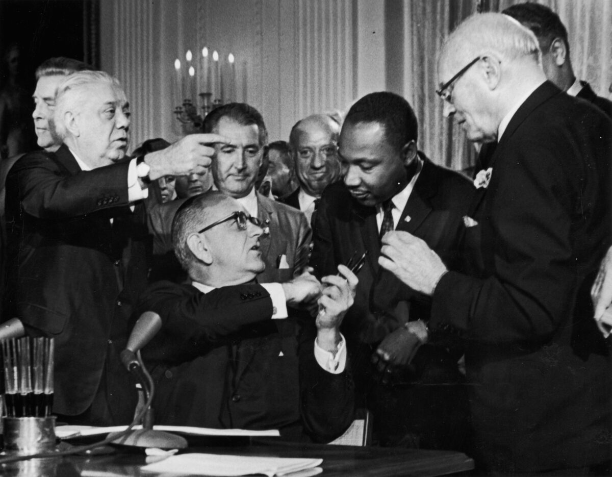 Tổng thống Lyndon B. Johnson bắt tay Tiến sĩ Martin Luther King Jr. tại lễ ký kết Đạo luật Dân quyền trước sự chứng kiến của các quan chức tại Hoa Thịnh Đốn hôm 02/07/1964. (Ảnh: Hulton Archive/Getty Images)