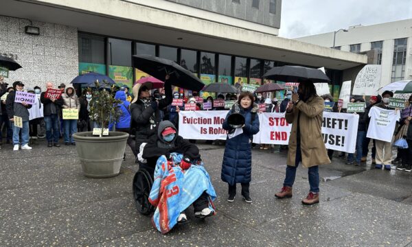 Hàng chục người giơ biển phản đối lệnh cấm trục xuất trong khi một chủ sở hữu nhà ở ngồi trên xe lăn tiếp tục tuyệt thực ở Oakland, California, hôm 26/02/2023. (Ảnh: Xue Mingzhu/The Epoch Times)