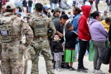 Các nhân viên và quan chức chấp pháp liên bang đang theo dõi trong khi những người nhập cư xếp hàng để được chở đi từ một trại tạm bợ giữa các bức tường biên giới Hoa Kỳ-Mexico ở San Diego hôm 13/05/2023. (Ảnh: Mario Tama/Getty Images)