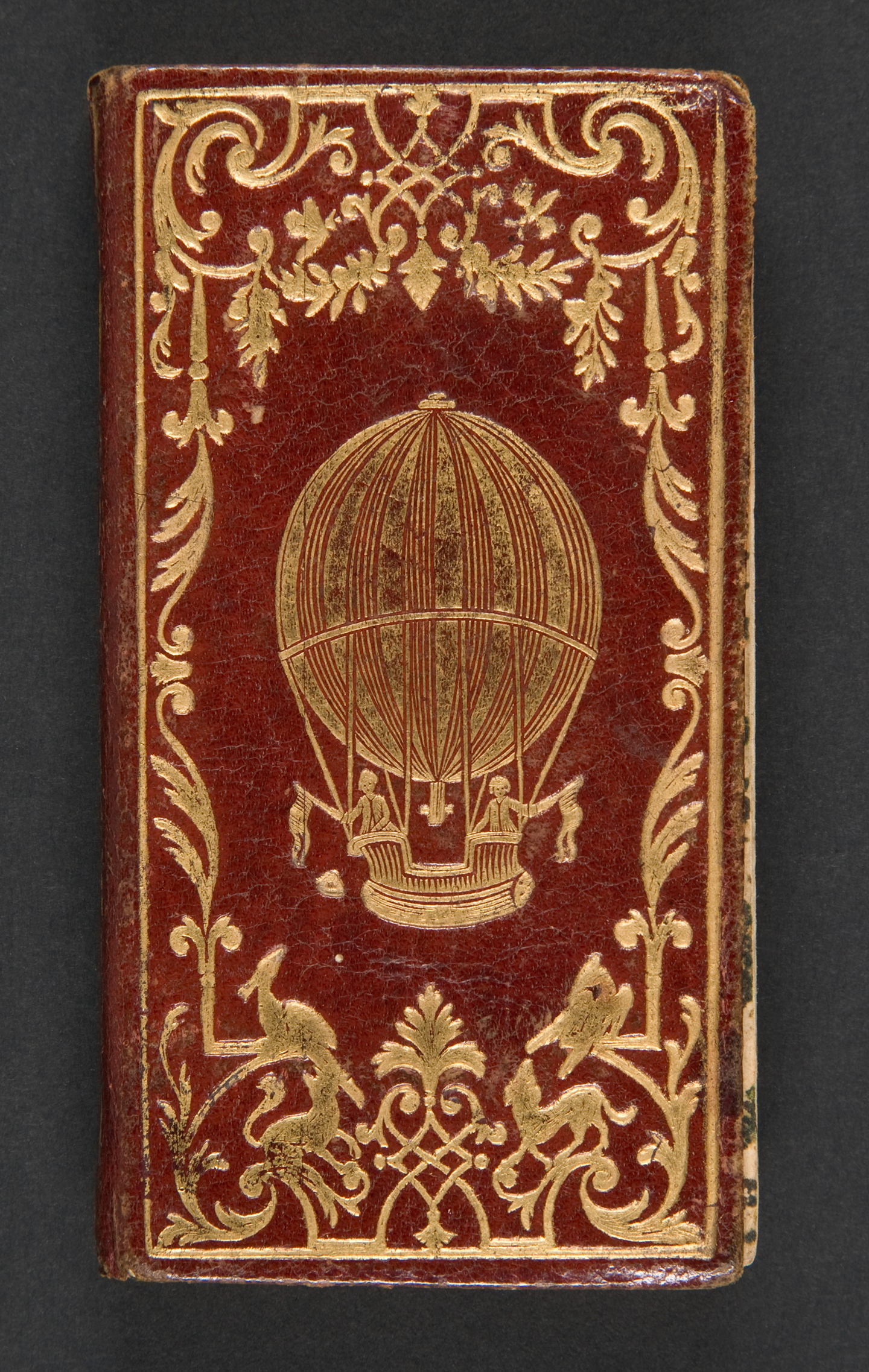 Bìa trước của cuốn sách “Le Calendrier de la Cour,” năm 1784, do Chez La Veuve Hérissant in và Jacques Collombat sáng tác. Bìa sách Morocco màu đỏ đương thời, khung viền mạ vàng tinh xảo với hình khinh khí cầu mạ vàng; kích thước: 4 5/16 inch. Món quà của bà Jayne Wrightsman, Bảo tàng Nghệ thuật Metropolitan, Thành phố New York. (Ảnh: Tài liệu công cộng)