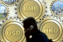 Một khách bộ hành đi ngang qua một biển quảng cáo có hình đồng nhân dân tệ Trung Quốc (RMB, trên cùng ở giữa), dollar Hồng Kông (HKD, bên phải), và dollar Mỹ (USD) được trưng bày trước một tòa nhà ở Hồng Kông hôm 21/03/2009. (Ảnh: Ted Aljibe/AFP qua Getty Images)