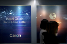 Các nhân viên đi ngang qua một biển quảng cáo tại văn phòng của Tài Tân (Caixin Media) ở Bắc Kinh vào ngày 18/01/2018. (Ảnh: Mark Schiefelbein/AP Photo)