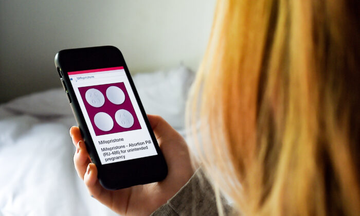 Một người phụ nữ nhìn vào viên thuốc phá thai—RU-486, hay mifepristone—trên điện thoại, ở Arlington, Virginia, vào ngày 08/05/2020. (Ảnh: Olivier Douliery/AFP qua Getty Images)