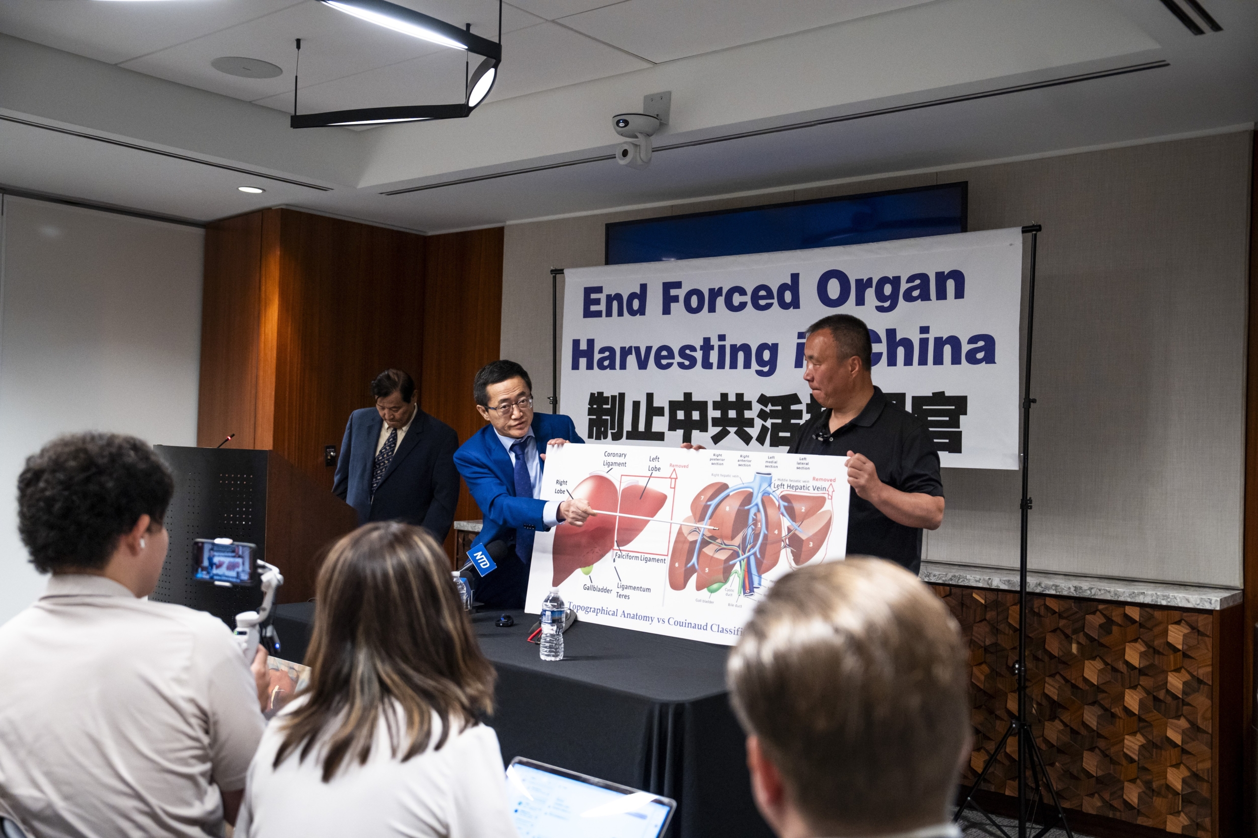 Bác sỹ Lý Tường Xuân (áo xanh) đang phân tích cấu trúc gan tại cuộc họp báo. Phía bên trái của biểu đồ là thùy trái và phải của gan; phía bên phải là các vùng của gan. (Ảnh: Madalina Vasiliu/The Epoch Times)