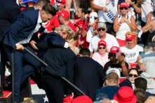 Ứng cử viên Đảng Cộng Hòa Donald Trump với vết máu trên mặt được các nhân viên mật vụ bao quanh khi ông được đưa ra khỏi sân khấu tại một sự kiện tranh cử tại Butler Farm Show Inc. ở Butler, Pennsylvania, hôm 13/07/2024. (Ảnh: Rebecca Droke/AFP qua Getty Images)