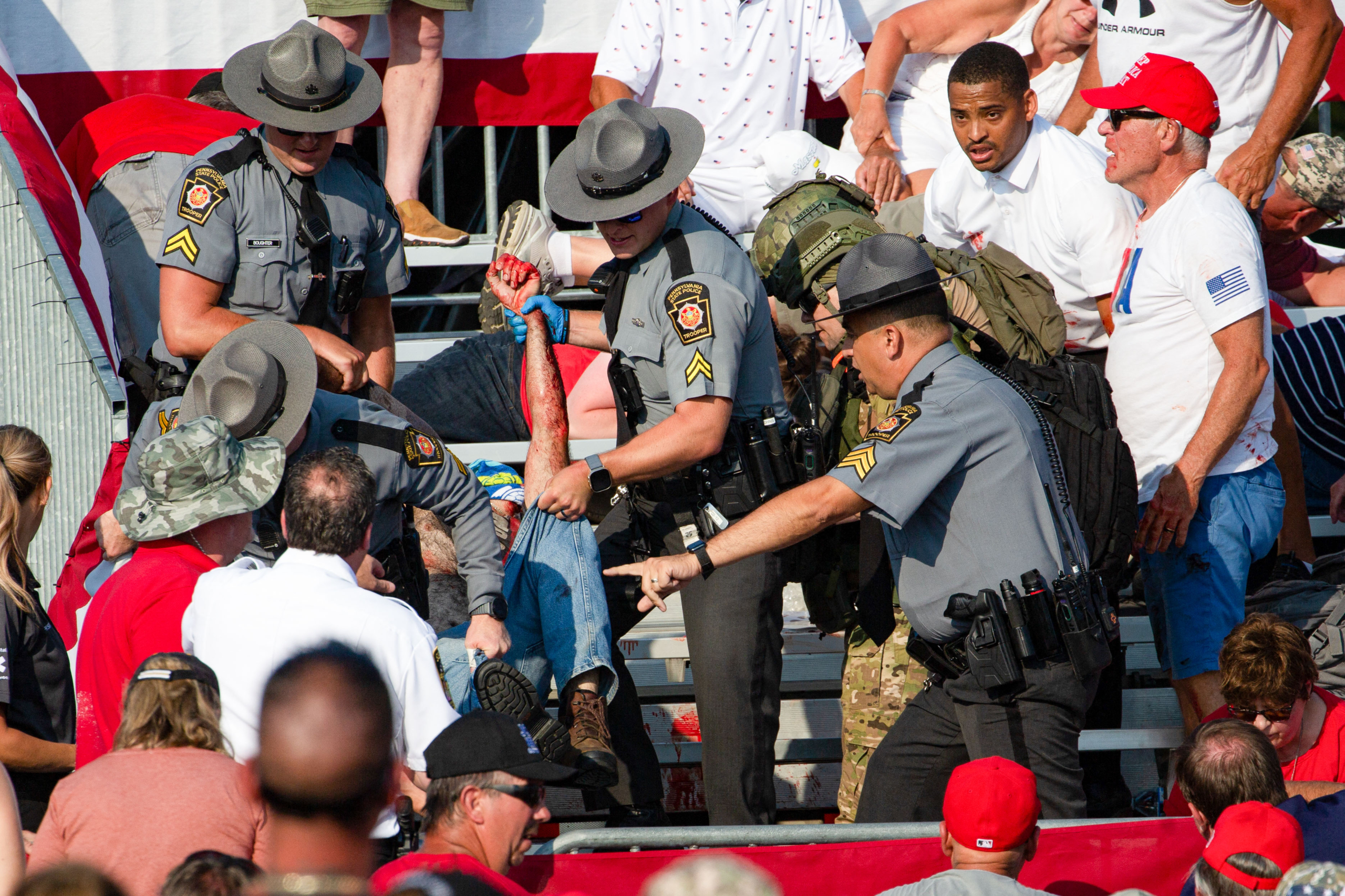 Cảnh sát đưa một người bị thương rời khỏi khán đài sau vụ nổ súng tại sự kiện vận động tranh cử. (Ảnh: Rebecca Droke/AFP qua Getty Images)